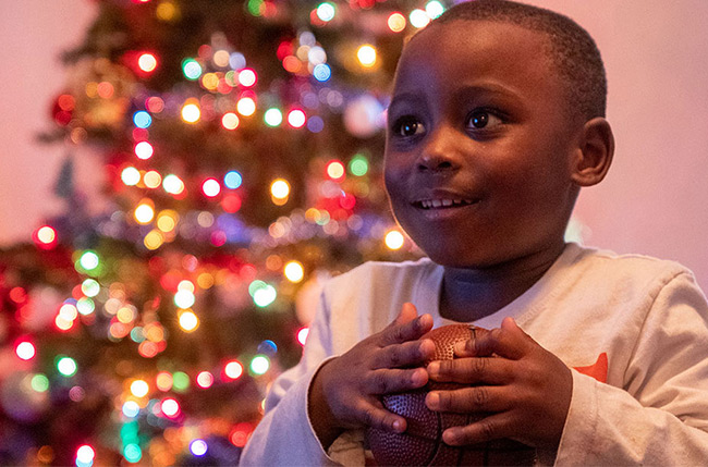 Child stands happily in front of his Christmas Tree with his new basketball.