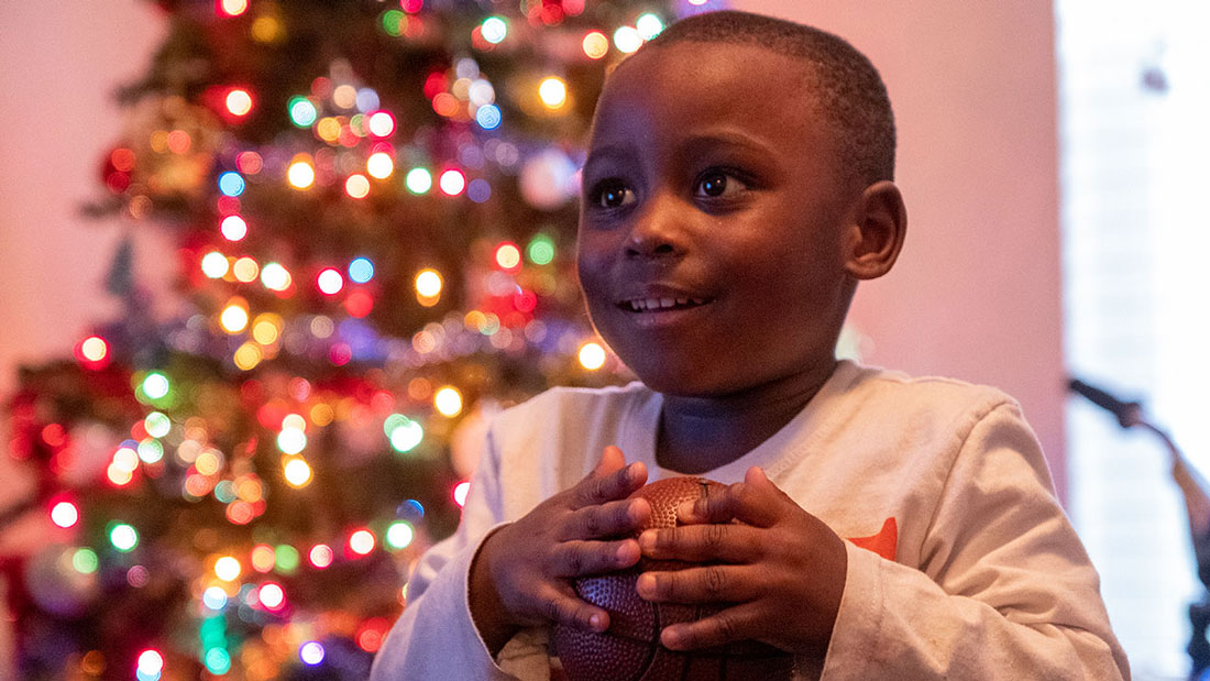 Child stands happily in front of his Christmas Tree with his new basketball.